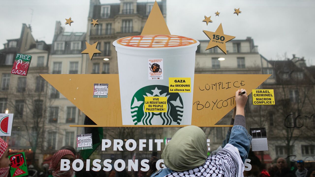 A woman writes "complicit" and "boycott" on a Starbucks window.